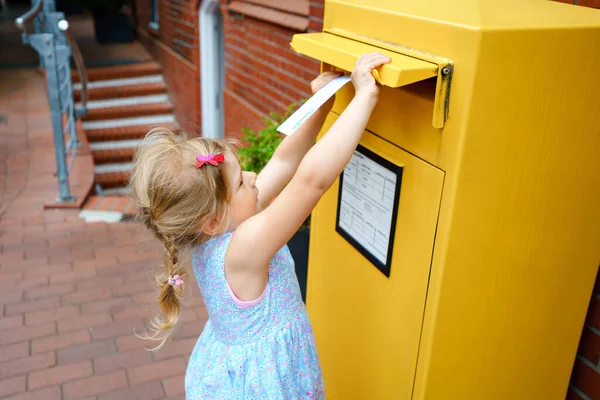 Una niña preescolar tirando cartas en un buzón. Emocionado niño escribiendo tarjeta o carta para abuelos o familiares. Forma de comunicación anticuada. — Foto de Stock