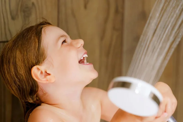 Een klein peutermeisje dat een bad neemt. Gelukkig gezond kleuter spelen met douchekop en water, plezier hebben. Wassen, schoonmaken, hygiëne voor kinderen. — Stockfoto