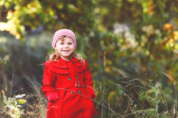 Nettes kleines Mädchen in rotem Mantel, das durch den herbstlichen Wald spaziert. Glückliches gesundes Baby, das mit seinen Eltern spazieren geht. Sonniger Herbsttag mit Kind. Aktive Freizeit und Aktivität mit Kindern in der Natur. — Stockfoto