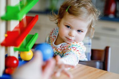 Küçük kız evde ya da çocuk odasında eğitici oyuncaklarla oynuyor. Mutlu sağlıklı çocuk renkli tahta top pisti ile eğleniyor. Çocuk top tutmayı ve yuvarlanmayı öğreniyor. Motorik eğitim.
