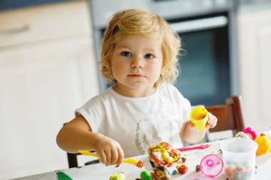 Renkli killi, sevimli, küçük bir kız. Sağlıklı bebek oyun oynuyor ve oyun hamurundan oyuncaklar yapıyor. Küçük çocuk kil kalıp ve öğrenim