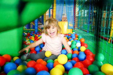Kapalı alanda oynayan aktif küçük bir kız. Neşeli anaokulu çocukları tırmanıyor, koşuyor, zıplıyor ve renkli plastik toplarla eğleniyor. Çocuklar için kapalı etkinlik.
