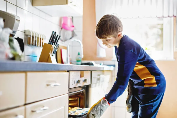 Happy blond school kid boy baking blueberry vanilla muffins in domestic kitchen, indoors. Funny lovely healthy child having fun with helping. — Stock Photo, Image