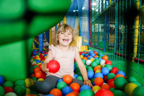 Ragazzina attiva che gioca nel parco giochi al coperto. Felice gioioso bambino in età prescolare arrampicata, corsa, salto e divertirsi con palline di plastica colorate. Attività all'aperto per bambini. — Foto Stock