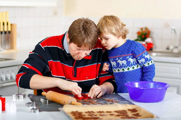 Petit garçon d'âge préscolaire et père cuisinant des biscuits au pain d'épice. Joyeux fils et père, homme en pull de Noël. Cuisine décorée pour Noël. Activité familiale de Noël — Photo