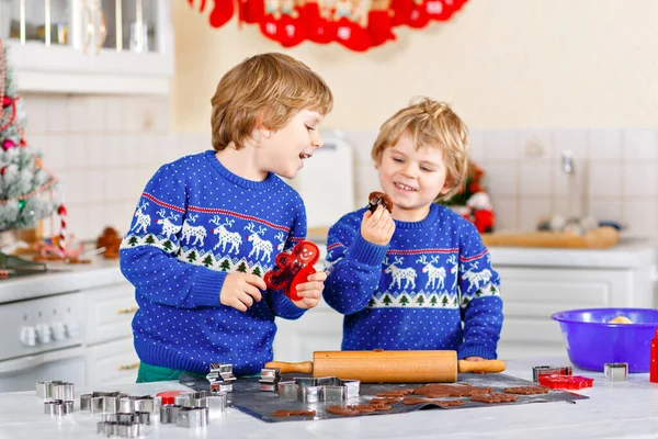 Zwei kleine Vorschulkinder backen Lebkuchen. Glückliche Geschwister, Kinder in Weihnachtspullovern. Weihnachtlich dekorierte Küche. Brüder, die kämpfen und Chaos stiften. Familienaktivitäten zu Weihnachten — Stockfoto