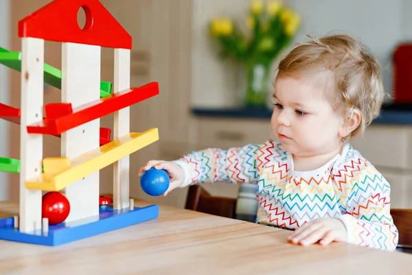 Little baby girl playing with educational toys at home or nursery. Happy healthy toddler child having fun with colorful wooden toy ball track. Kid learning to hold and roll balls. Motoric education. — Stock Photo, Image
