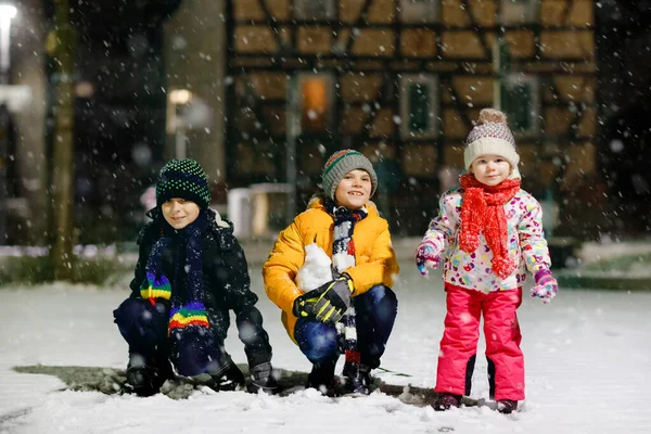 Dwóch małych chłopców i słodkie dziecko dziewczyna siedzi razem bawiąc się śniegiem w zimową noc. Rodzeństwo, bracia i siostrzyczka cieszą się silnymi opadami śniegu. Aktywna zabawa na rodzinne wakacje — Zdjęcie stockowe