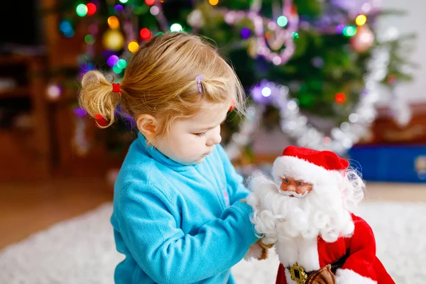 Rozkošné batole, co si hraje s dárky a vánočními hračkami. Malé dítě se baví s dekorovaným a osvětleným stromem Xmas se světly na pozadí. Šťastná zdravá holčička. — Stock fotografie