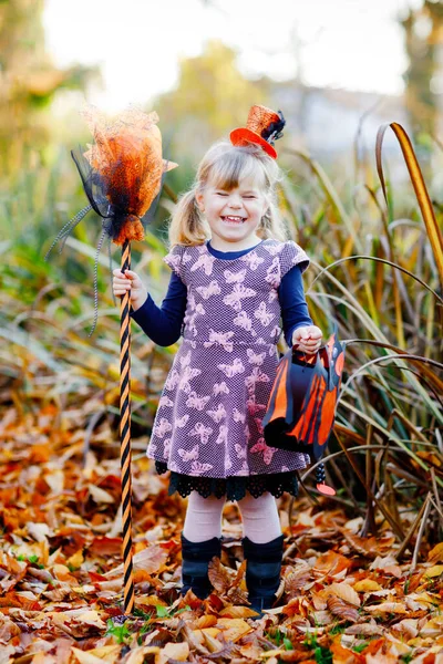 Милая маленькая девочка, одетая как ведьма, празднует Хэллоуин. Счастливый ребенок на улице, в оранжевой смешной шляпе и с ведьминской метлой и мешком от летучих фонарей. Прекрасный семейный фестиваль в октябре. — стоковое фото