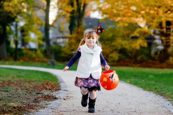 Liten småflicka klädd som ett häxtrick eller godis på Halloween. Glad barn utomhus, med orange rolig hatt och pumpa väska för söt hemsökelse. Familjefestivalsäsong i oktober. Friluftsliv — Stockfoto