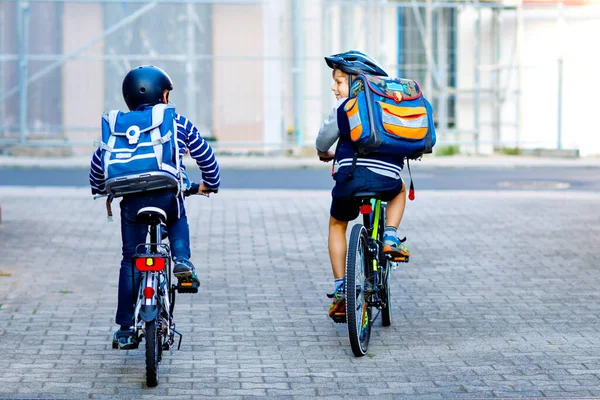 Två skolpojkar i skyddshjälm rider med cykel i staden med ryggsäckar. Glada barn i färgglada kläder cykling på cyklar på väg till skolan. Säkert sätt för barn utomhus till skolan — Stockfoto