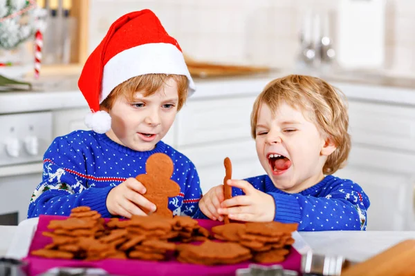 Zwei kleine Vorschulkinder backen Lebkuchen. Glückliche Geschwister, Kinder in Weihnachtspullovern. Weihnachtlich dekorierte Küche. Brüder, die kämpfen und Chaos stiften. Familienaktivitäten zu Weihnachten — Stockfoto