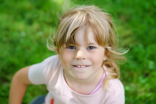 Egy boldog mosolygós óvodás lány portréja a szabadban. Egy szőke hajú kisgyerek, aki a kamerába néz és mosolyog. Boldog egészséges gyermek élvezze a szabadtéri tevékenység és a játék. — Stock Fotó