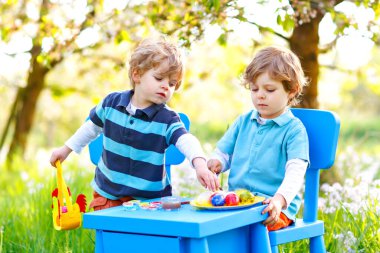 İki küçük çocuk Paskalya tavşanı kulakları takıyor, renkli yumurta boyuyorlar.