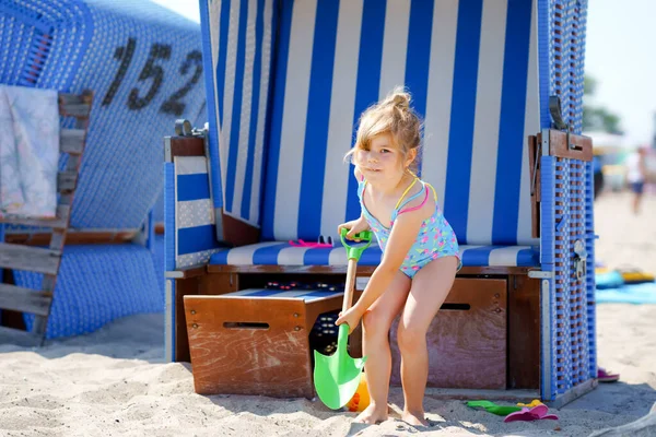 Niña preescolar jugando con juguetes de arena en la playa. Lindo niño feliz en vacaciones familiares en el mar. Niño cerca de la silla de playa de mimbre techado en el Mar Báltico. Actividad al aire libre para niños —  Fotos de Stock