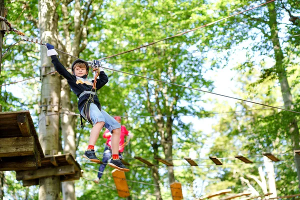 Niño en el parque de aventura forestal. El chico con casco trepa por un sendero de cuerda alta. Habilidades de agilidad y escalada al aire libre centro de atracciones para niños. Actividad al aire libre para niños y familias. — Foto de Stock