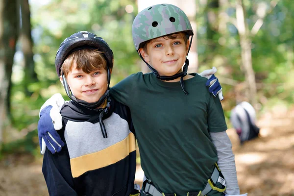 Duas crianças no parque de aventura florestal. Crianças meninos de capacete sobe em trilha corda alta. Habilidades de agilidade e escalada centro de diversões ao ar livre para crianças. Atividades ao ar livre para crianças e famílias. — Fotografia de Stock