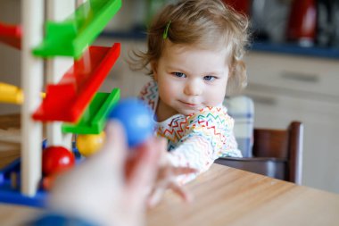 Küçük kız evde ya da çocuk odasında eğitici oyuncaklarla oynuyor. Mutlu sağlıklı çocuk renkli tahta top pisti ile eğleniyor. Çocuk top tutmayı ve yuvarlanmayı öğreniyor. Motorik eğitim.