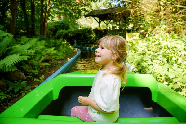 Adorable little toddler girl riding on boat carousel in amusement park. Happy healthy baby child having fun outdoors on sunny day. Family weekend or vacations — Stock Photo, Image