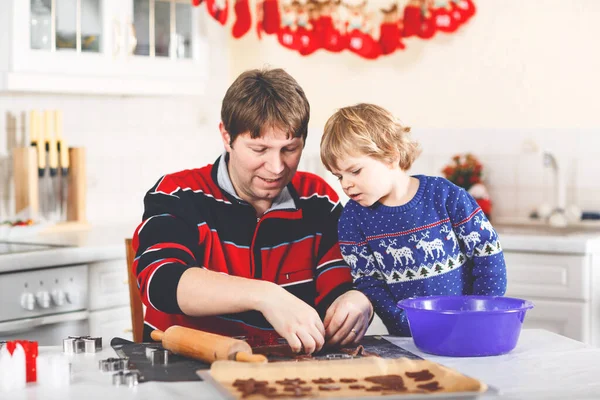 Băiatul preşcolar şi tata copt prăjituri cu turtă dulce. Fericit fiu și tată, om în pulovere de Crăciun. Bucătărie decorată de Crăciun. Activitatea familiei de Crăciun — Fotografie, imagine de stoc