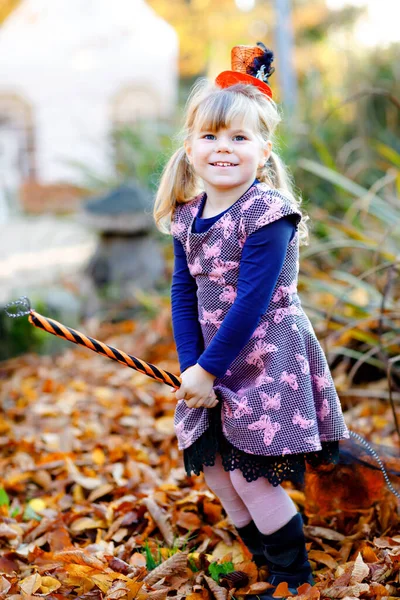 Roztomilé malé batole dívka oblečená jako čarodějnice slaví Halloween. Šťastné dítě venku, s oranžovým legračním kloboukem a koštětem. Krásná rodinná slavnostní sezóna v říjnu. Venkovní aktivita — Stock fotografie