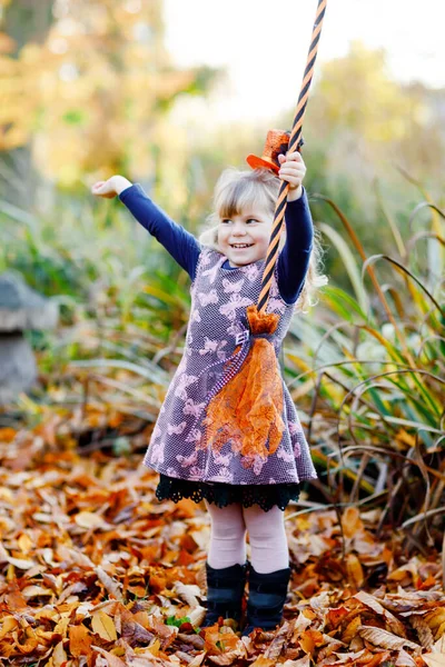 Menina bonito pequena criança vestida como uma bruxa celebra o Halloween. Criança feliz ao ar livre, com chapéu laranja engraçado e segure vassoura bruxa. Bela temporada de festivais de família em outubro. Actividade exterior — Fotografia de Stock