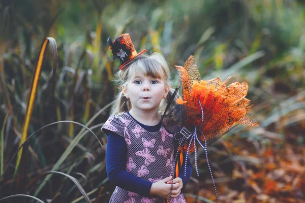 Portrait of little toddler girl dressed as a witch celebrates Halloween. Happy child outdoors, with orange funny hat and hold witch broom. Beautiful family festival season in october. Outdoor activity — Stock Photo, Image