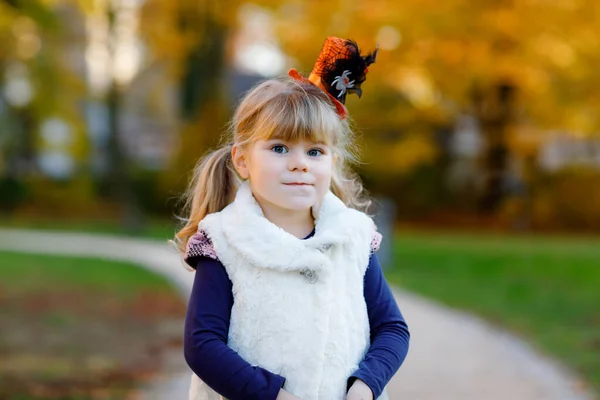 El retrato de una niña pequeña vestida de bruja celebra Halloween. Niño feliz al aire libre, con sombrero divertido naranja en el cálido día de otoño. Hermosa temporada de festivales familiares en octubre. Actividades al aire libre —  Fotos de Stock