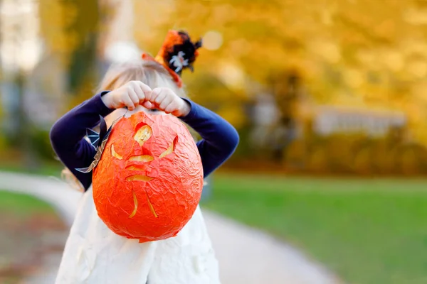 Malá batolátko dívka oblečená jako čarodějnice trik nebo dárek na Halloween. Šťastné dítě venku, s pomerančovou legrační čepicí a dýňovou taškou na sladké strašení. Rodinná sezóna v říjnu. Nerozpoznatelná tvář — Stock fotografie