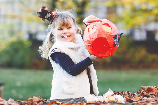 Little toddler girl dressed as a witch trick or treating on Halloween. Happy child outdoors, with orange funny hat and pumpkin bag for sweet haunt. Family festival season in october. Outdoor activity — Stock Photo, Image