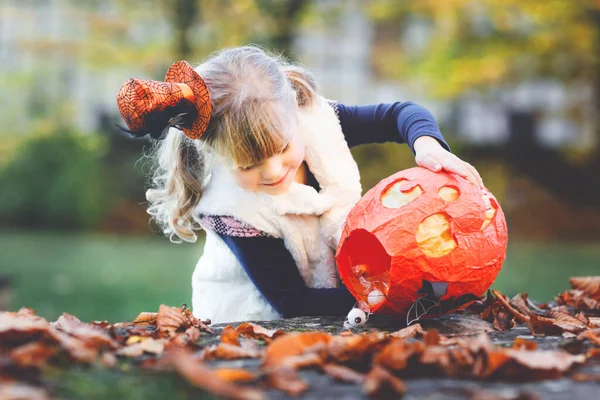 Little toddler girl dressed as a witch trick or treating on Halloween. Happy child outdoors, with orange funny hat and pumpkin bag for sweet haunt. Family festival season in october. Outdoor activity — Stock Photo, Image