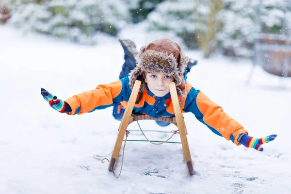 Menino que gosta de andar de trenó durante a queda de neve. Um miúdo pré-escolar feliz a andar de trenó vintage. Criança brincar ao ar livre com neve. Diversão ativa para férias de Natal em família no inverno — Fotografia de Stock