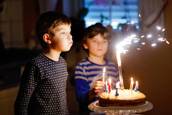 Two beautiful kids, little preschool boys celebrating birthday and blowing candles on homemade baked cake, indoor. Birthday party for siblings children. Happy twins about gifts and fireworks on tarte. — Stock Photo, Image