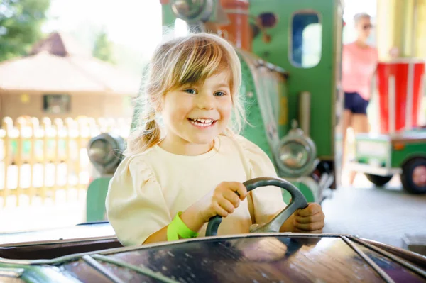 Adorable petite fille en bas âge chevauchant sur carrousel rond-point dans un parc d'attractions. Bébé enfant en bonne santé heureux de s'amuser à l'extérieur le jour ensoleillé. Week-end en famille ou vacances — Photo