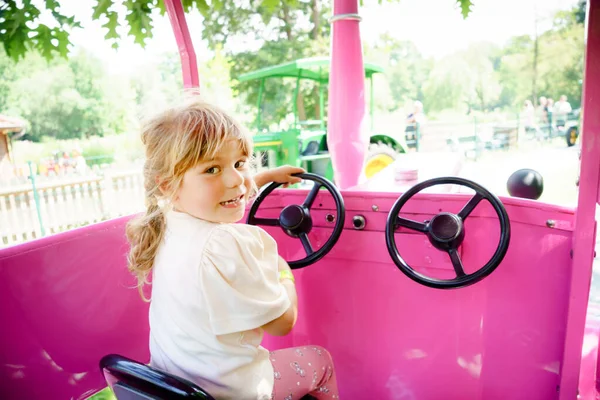 Adorabile bambina che cavalca su giostra rotonda nel parco divertimenti. Buon bambino sano divertirsi all'aperto nella giornata di sole. Weekend in famiglia o vacanze — Foto Stock