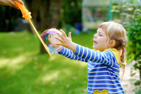 Boldog kis szőke óvodás lány szórakozik szappanbuborék fúvóval. Aranyos gyerek játszik a napos nyári napon. Boldog, aktív, vicces, egészséges gyereket. Tevékenység gyermekek számára. — Stock Fotó