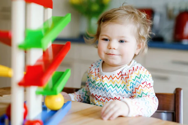 Pequena menina brincando com brinquedos educativos em casa ou berçário. Criança infantil saudável feliz se divertindo com pista de bola de brinquedo de madeira colorida. Criança aprendendo a segurar e rolar bolas. Ensino motorizado. — Fotografia de Stock