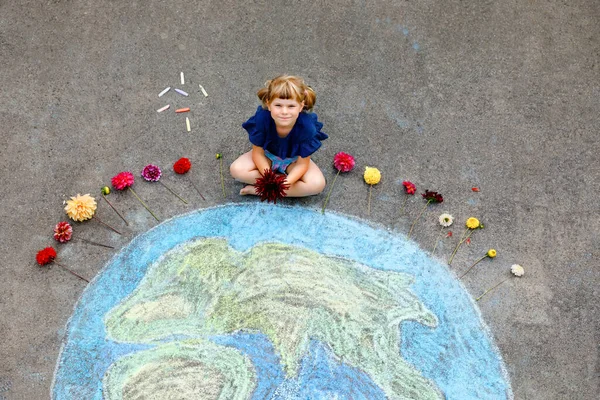 Little preschool girl with flowers and earth globe painting with colorful chalks on ground. Positive toddler child. Happy earth day concept. Creation of children for saving world, environment and