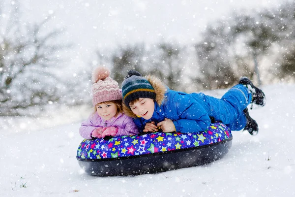 Active toddler girl and school boy sliding together down the hill on snow tube. Happy children, siblings having fun outdoors in winter on sledge. Brother and sister tubing snowy downhill, family time. — Stock Photo, Image