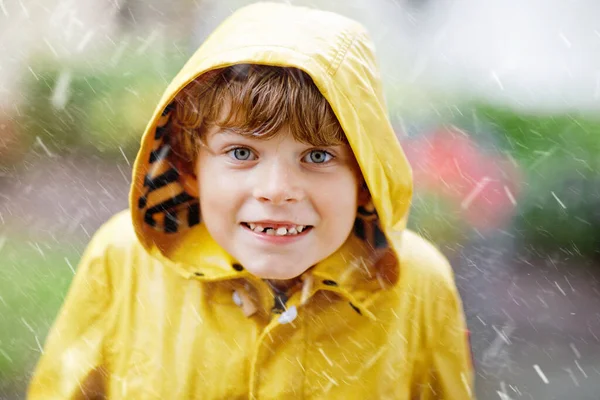 Beautiful little kid boy on way to school walking during sleet, heavy rain and snow with an umbrella on cold day. Happy and joyful child in colorful yellow coat fashion casual clothes — Stock Photo, Image