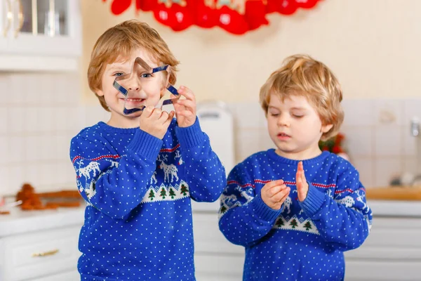 Két óvodás fiú mézeskalács sütit süt. Boldog testvérek, gyerekek karácsonyi pulóverben. Konyha díszítve karácsonyra. Testvérek harcolnak, zűrzavart okoznak. Karácsonyi családi tevékenység — Stock Fotó