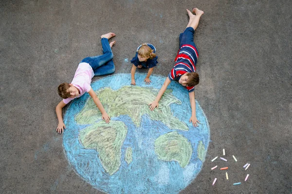 Niña preescolar y dos niños de la escuela con la pintura globo de tierra con tiza de colores en el suelo. Feliz concepto del día de la tierra. Creación de niños para salvar el mundo, el medio ambiente y la ecología. —  Fotos de Stock