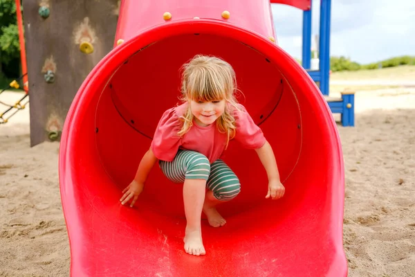 Little preschool girl playing on outdoor playground. Happy toddler child climbing and having fun with summer outdoors activity. Girl slinding down the slide. Children having fun. — Stock Photo, Image