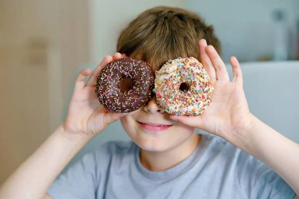 Menino da escola pré-adolescente feliz comendo donut doce em casa. Criança loira na cozinha doméstica ou na cantina da escola Criança bonito e comida açucarada insalubre. — Fotografia de Stock