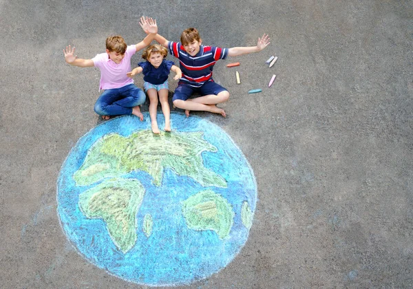 Niña preescolar y dos niños de la escuela con la pintura globo de tierra con tiza de colores en el suelo. Feliz concepto del día de la tierra. Creación de niños para salvar el mundo, el medio ambiente y la ecología. —  Fotos de Stock