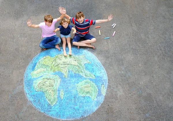 Little preschool girl and two school kids boys with earth globe painting with colorful chalks on ground. Happy earth day concept. Creation of children for saving world, environment and ecology.