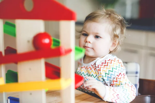 Niña jugando con juguetes educativos en casa o guardería. Feliz niño sano que se divierte con colorida pista de bolas de juguete de madera. Niño aprendiendo a sostener y rodar bolas. Educación automovilística. — Foto de Stock