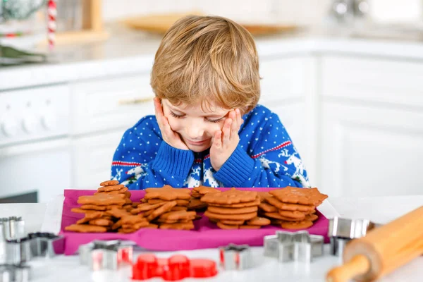 Malý předškolák peče perníkové sušenky. Šťastné aktivní batole dítě ve vánočním svetru. Kuchyně vyzdobená na Vánoce. Vánoční rodinná činnost — Stock fotografie