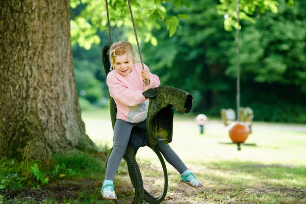 Menina pré-escolar pequena feliz se divertindo no balanço no jardim doméstico. Criança saudável balançando no dia de verão. Atividades infantis ao ar livre, criança sorrindo ativa rindo. Pneus velhos como balanço. — Fotografia de Stock